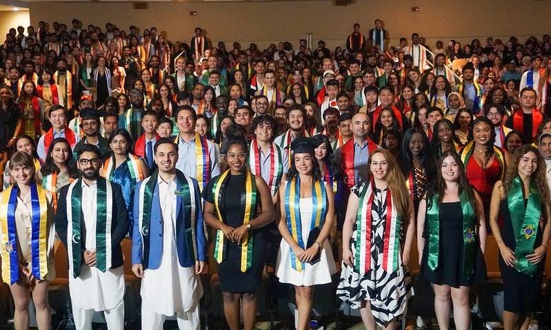 group photograph of USF international students stading as a group at their seats with their country sashes in the MSC Oval Theater auditorium