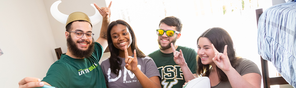 Four USF students taking a picture together while holding up the bulls sign.