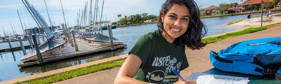 Female USF student doing schoolwork by the water 