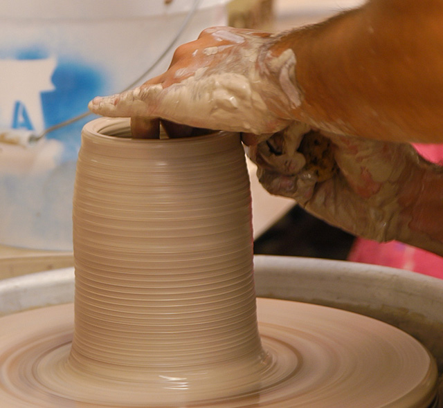 Student shapes a piece of clay on a potter's wheel.