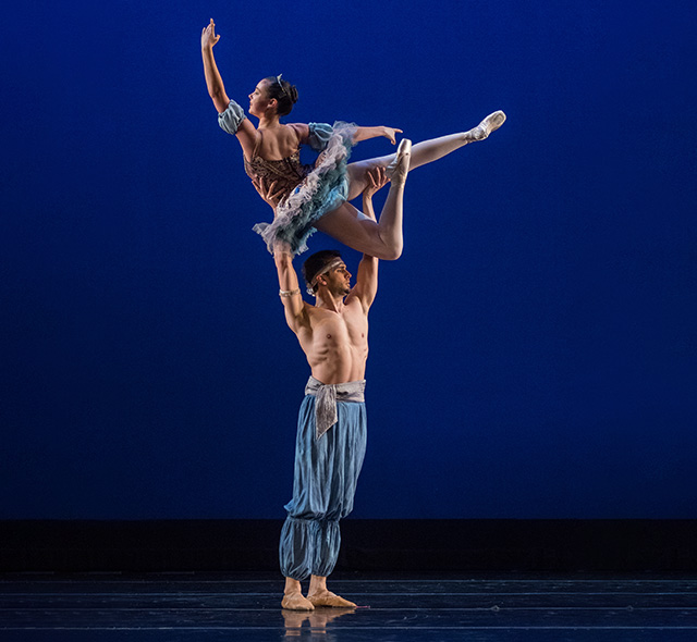 Dance students performing a ballet lift on stage.