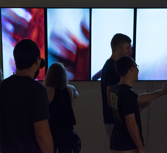 Students interacting with an exhibition display of MFA student video art.