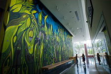 Two students talking in the Music Concert Hall lobby next to the mural by artist Janaina Tschäpe.
