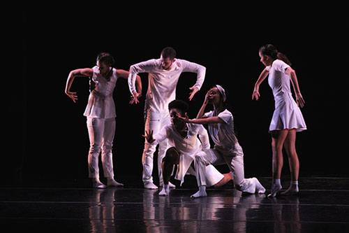 Five USF dance students are pictures in white clothing against a black background performing in the Fall 2017 Student Dance Concert
