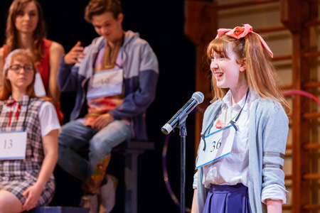 A student spells a word in front of a crowd in the performance of "The 25th Annual Putnam County Spelling Bee."