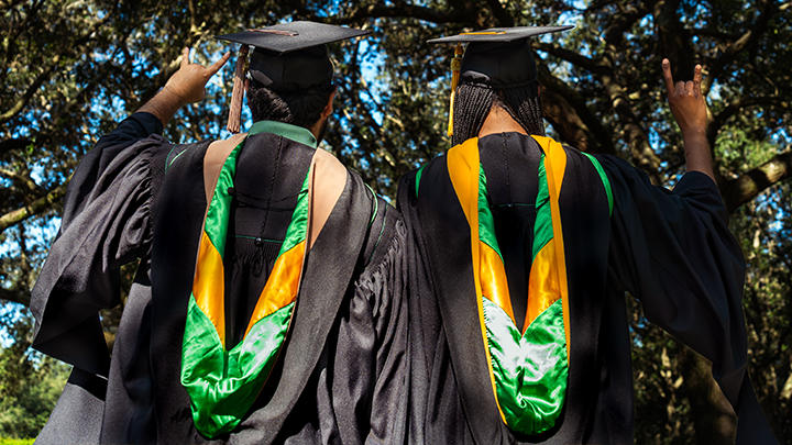Two USF grads, wearing regalia, shown from the back.