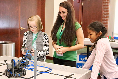 USF student shows elementary-aged students how to use a VEX robot