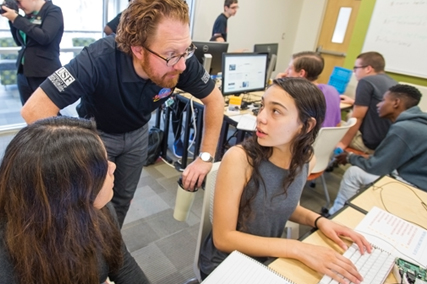 Male instructor explaining something to two female students at a computer.