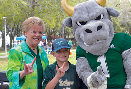 President Law, at left, poses with a little boy in a USF number one jersey and Rocky to the right make the USF bulls hand signal on a the MLK Plaza on a bright, sunny spring day at the first USF Family Fest.