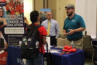 career fair table with two male recruiters chatting with female student