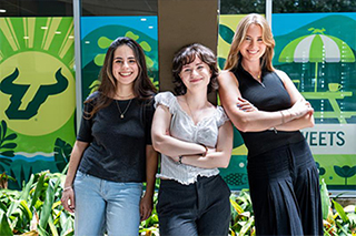 three female student interns standing in front of a brightly colored mural on the windows of Argos dining