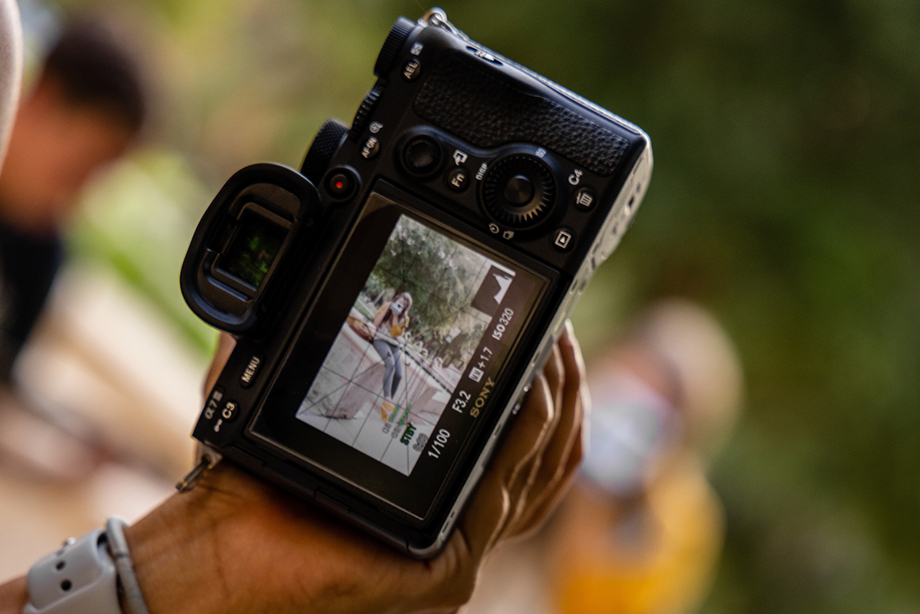 Person holding a DSLR camera with LCD screen as foreground and subject of photo in background. 