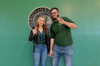 Honors student Alex Lewis and Honors Student Engagement Coordinator Daniel Woods pose in front of the USF seal while making a go Bulls sign