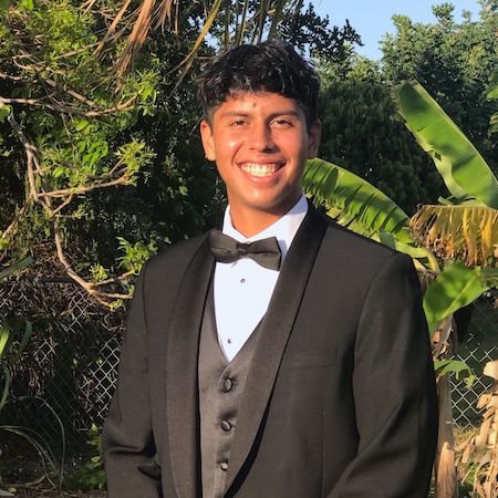 A man with short dark hair smiles in a black tuxedo