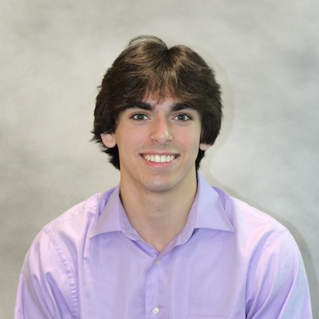 A man with long dark hair smiles in a purple collared shirt
