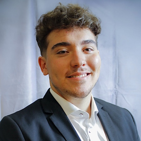 A man smiles in a white shirt and blue suit jacket