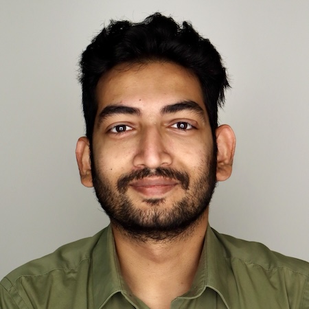 A man with dark hair and brown eyes smiles in a green shirt