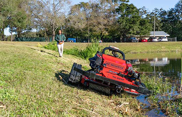 A remote controlled mower is being used to mow an embankment on a retention pond.