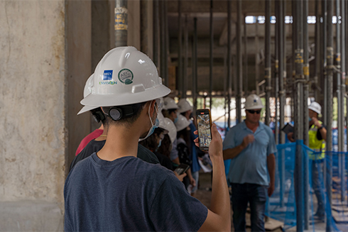 A student records the inside of the Judy Genshaft Honors college construction project as the project manager speaks in the background.