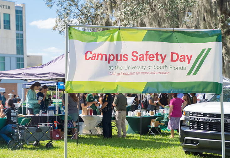 A banner that reads "Campus Safety Day at the University of South Florida" with a large crowd behind it in the event space.