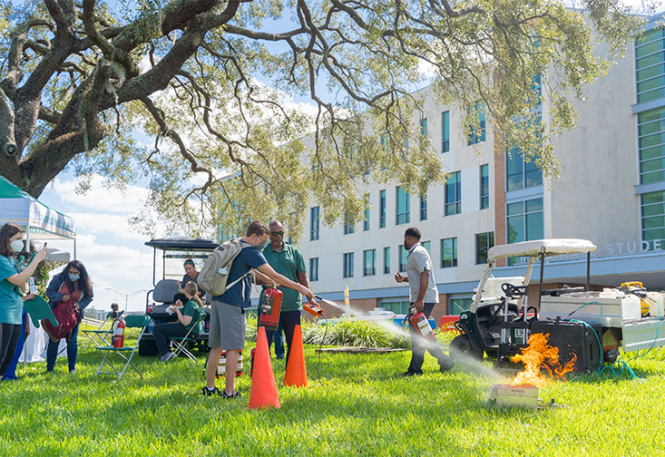 A student practices using a fire extingisher to put out a controlled fire with Environmental Health and Safety.