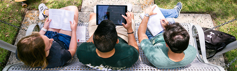 Three USF students sitting on a bench and preparing for class.