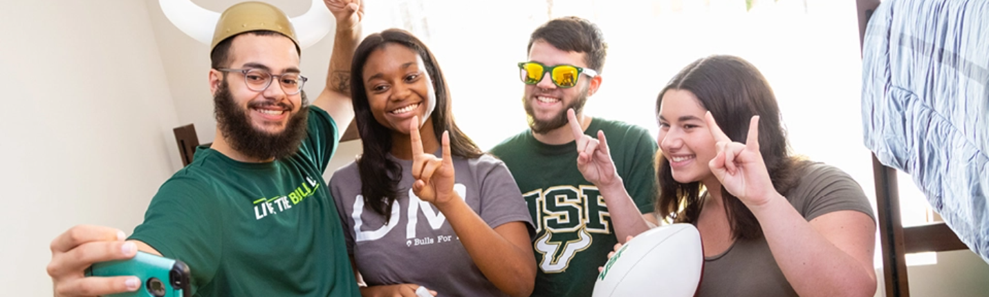Group of four USF students in a dorm room taking a photo after submitting their residency information.