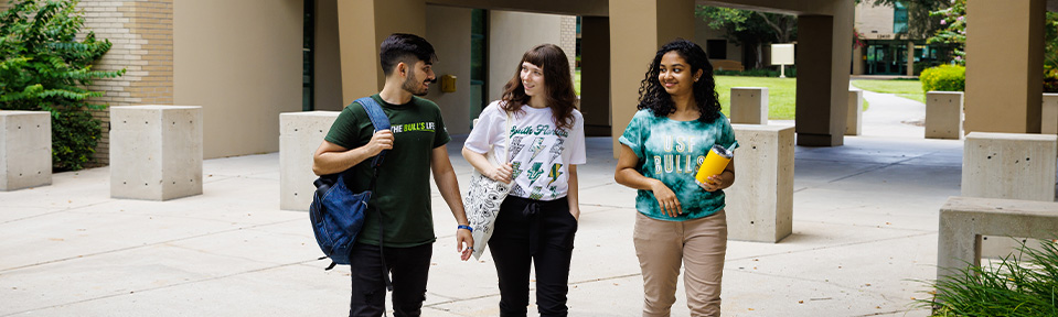 Three USF students walking by Castor Hall on campus.