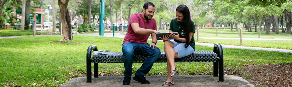 Two USF students sitting on a bench and using a tablet.