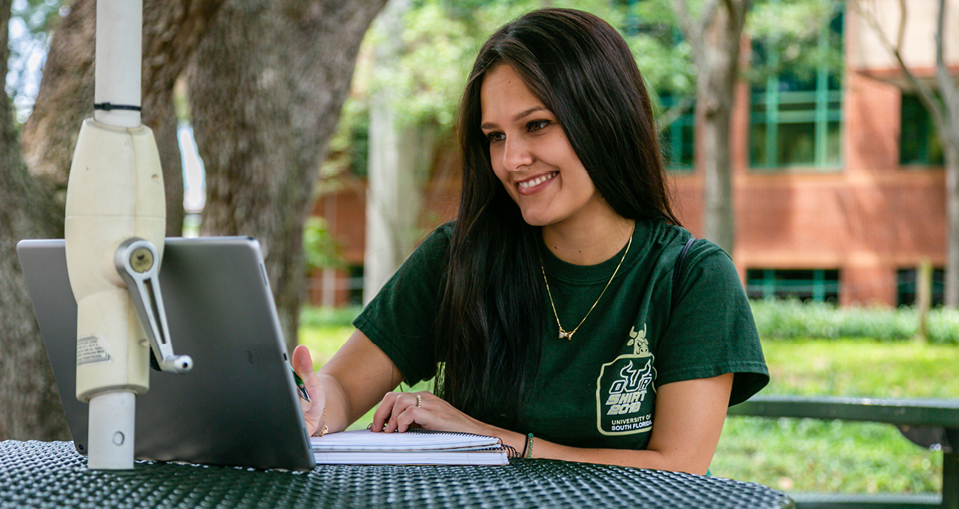 A female USF student sitting on campus taking notes.