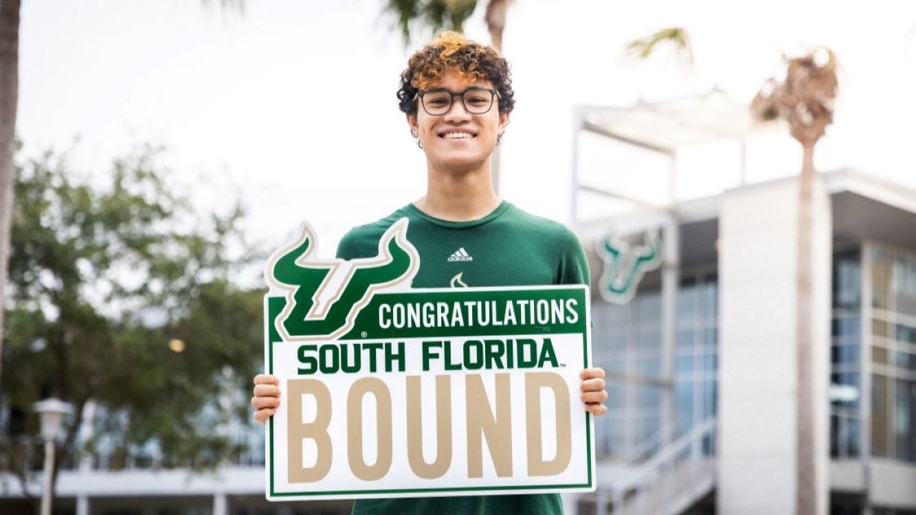 a USF student holding a sign that reads "Congratulations! South Florida Bound"