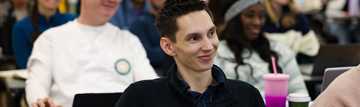 A USF student sitting in a lecture hall and smiling during class.