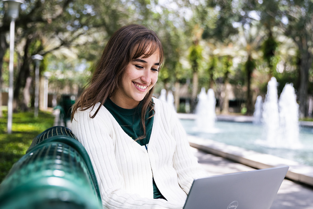 Student sitting on a bench and looking at their laptop.