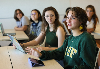 A group of USF students engaged in class and taking notes on their laptops and tablets.