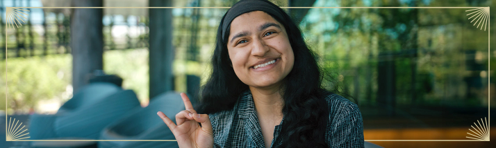 A USF National Merit Scholar smiling and holding up the Go Bulls hand symbol.