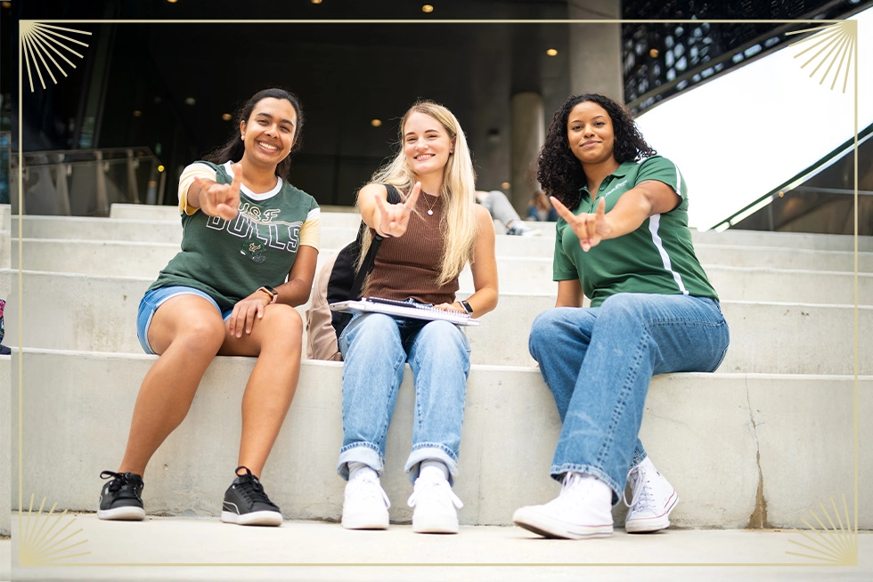 Three USF students smiling on campus.