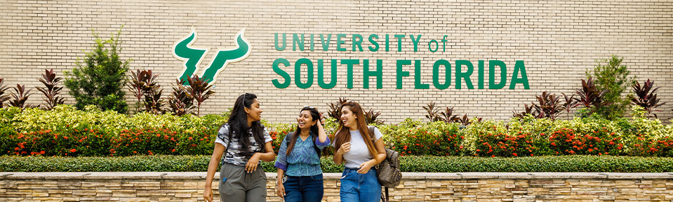 Three students walking by the University of South Florida sign on campus.