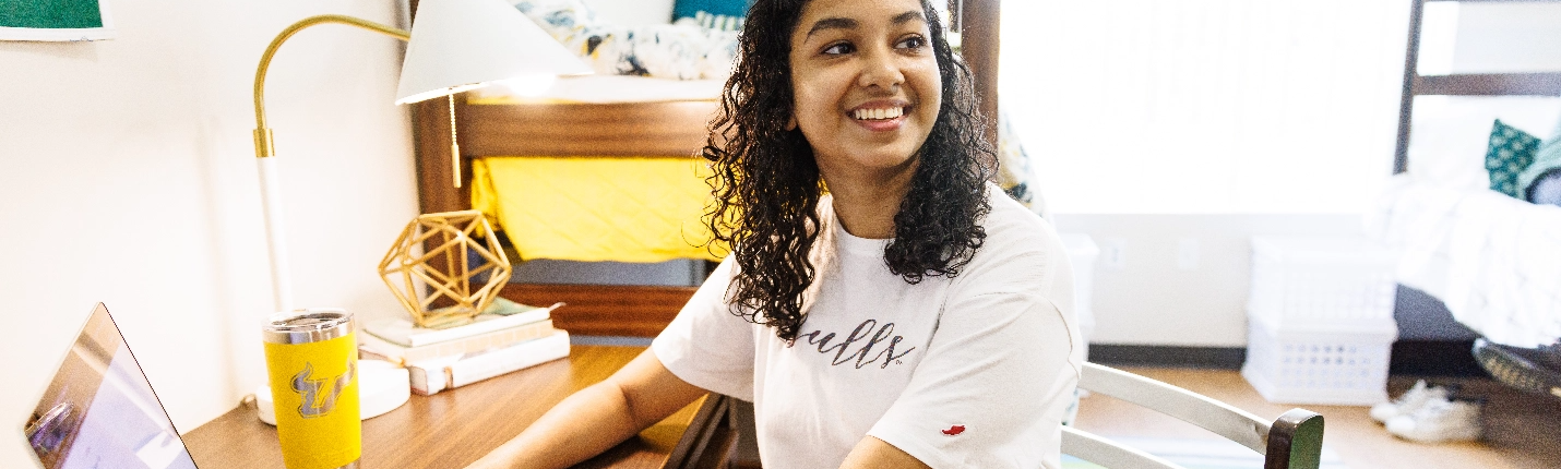 A USF student smiling in her dorm room.