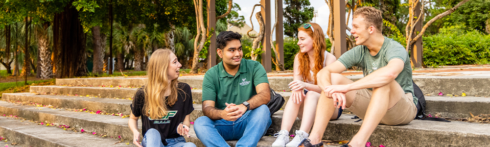 Four USF students sitting on stairs and chatting on campus.