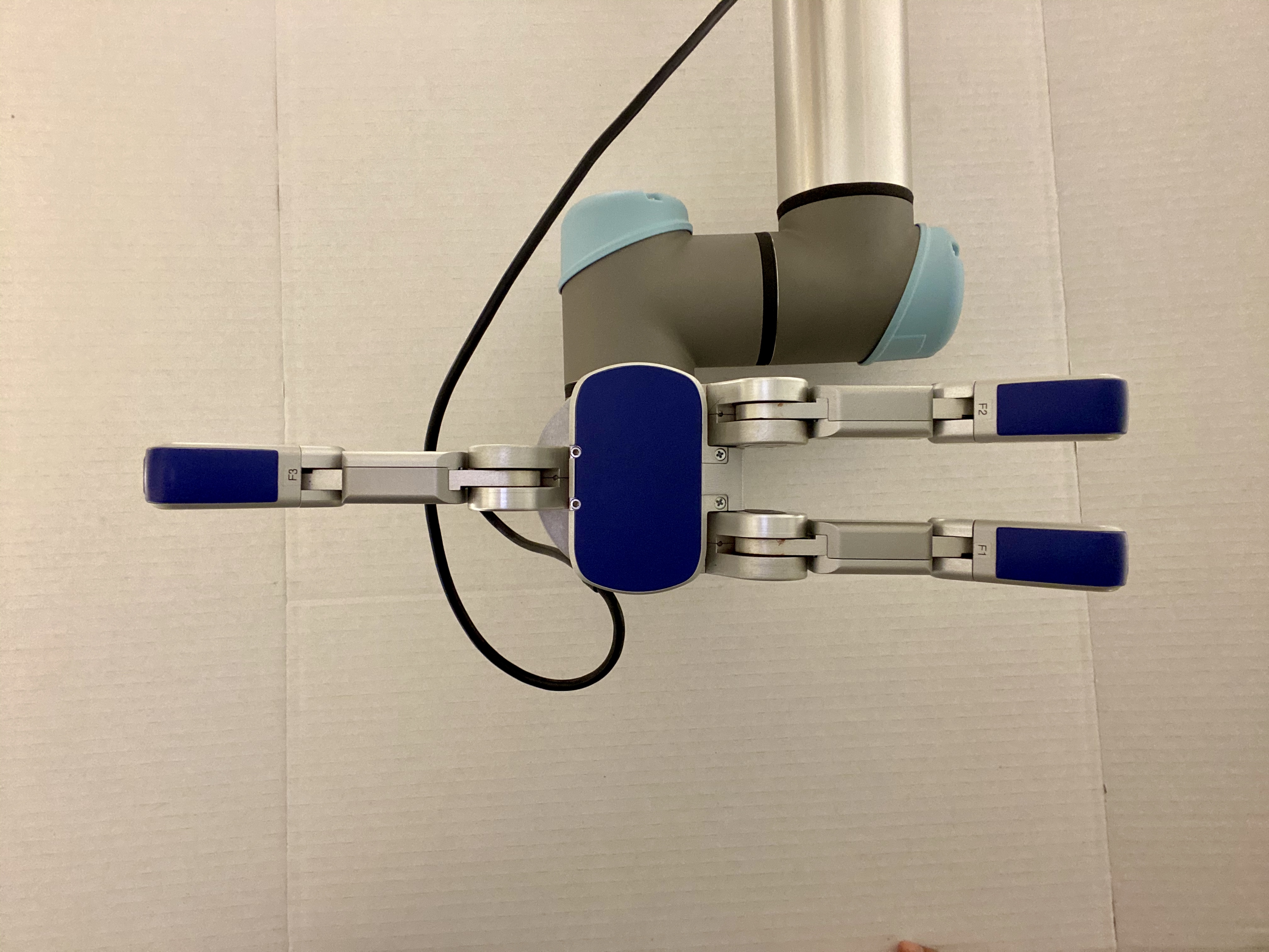 A robotic arm with a gray and blue design is positioned against a plain white background, featuring two blue grippers on either side. The arm's mechanical joints and cables are visible, highlighting a technology-focused setting.