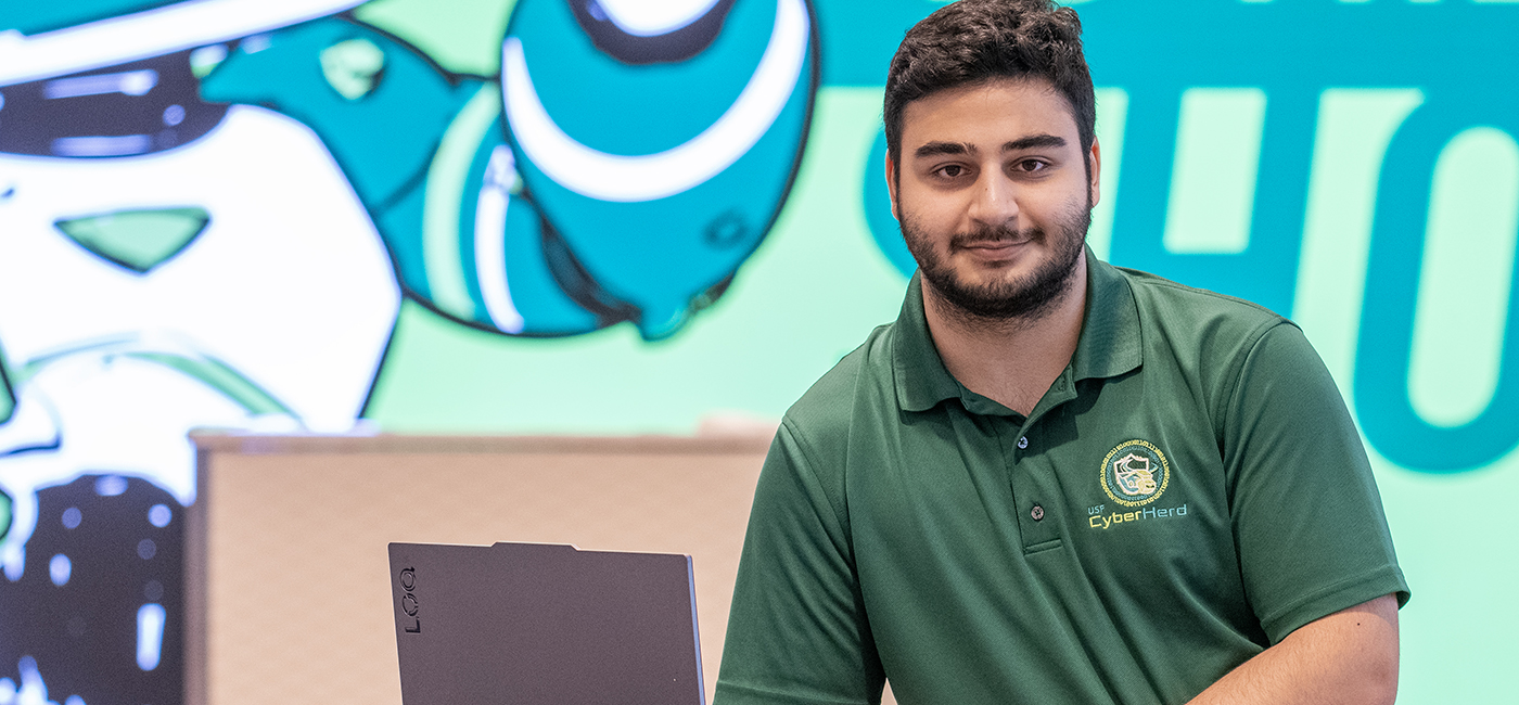 USF student Fagan Afandiyev, with his computer in the photo, turned an early passion for robotics competitions into a path toward a career in cybersecurity.