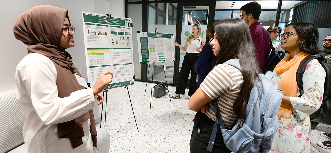 Bellini College students show off and explain their research posters at the AI+X Symposium.