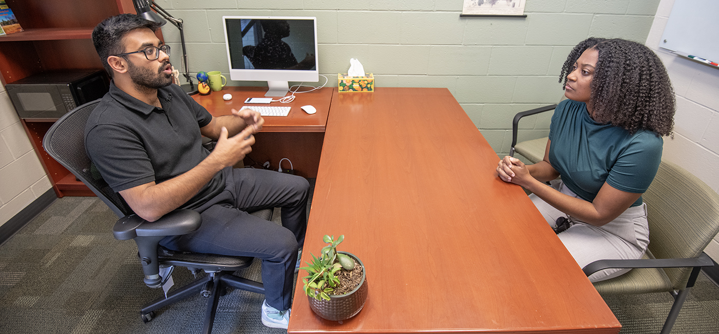 USF Bellini Assistant Professor Anshuman Chhabra sitting at a desk on the left talking to a reporter on the right side of the photo.
