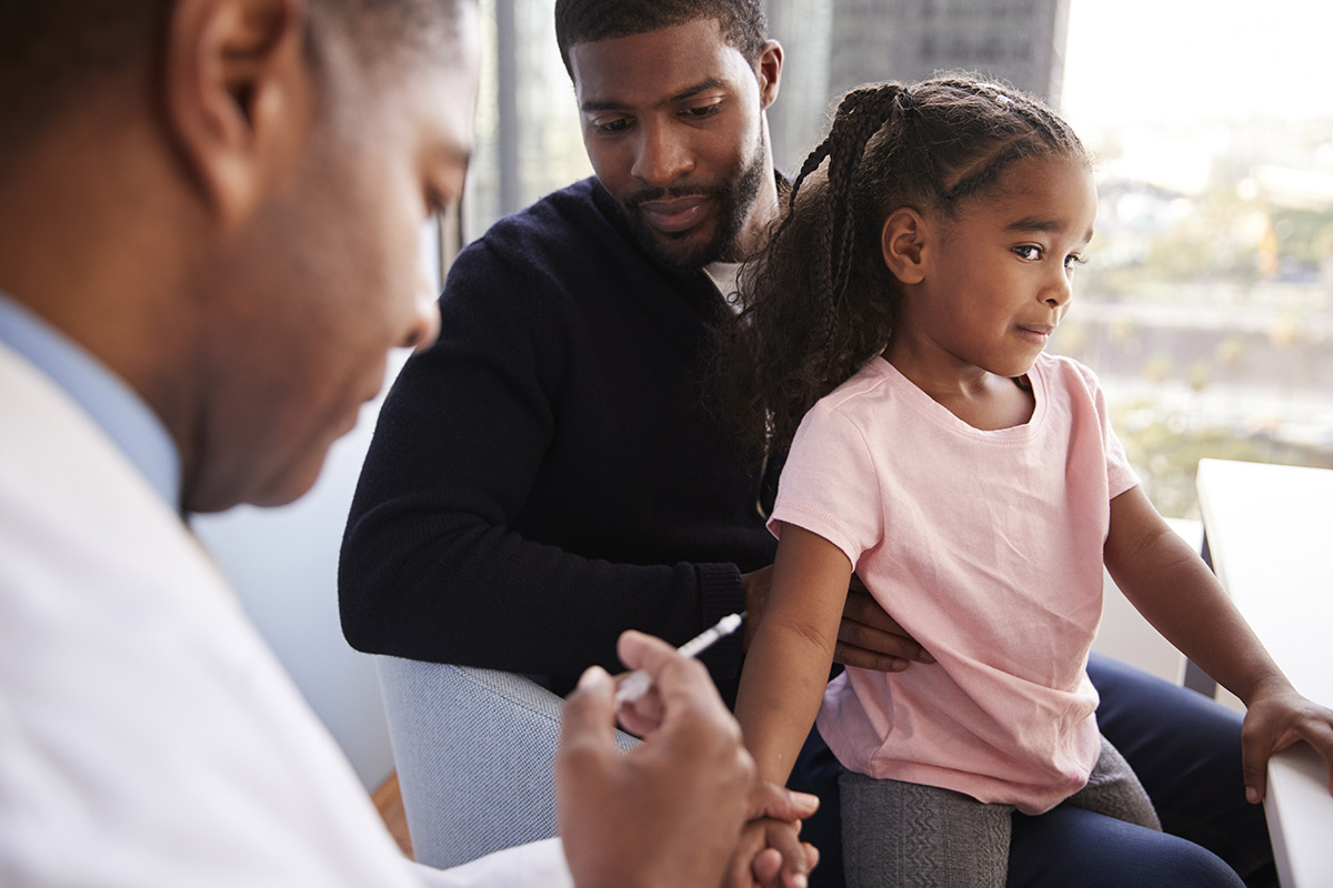 man holding girl who receives vaccine shot
