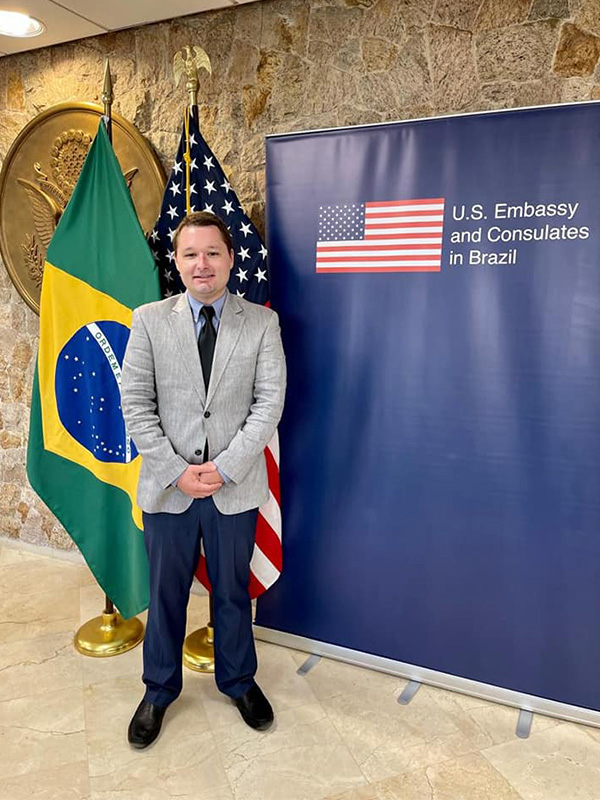 Josh Scacco standing in front of sign and flags