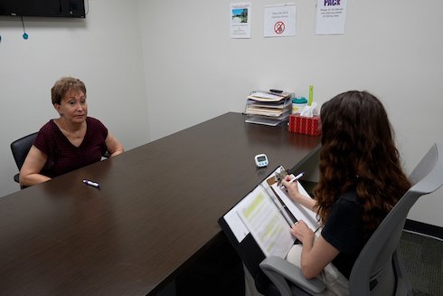 senior woman seated across a table from a person writing in a notebook