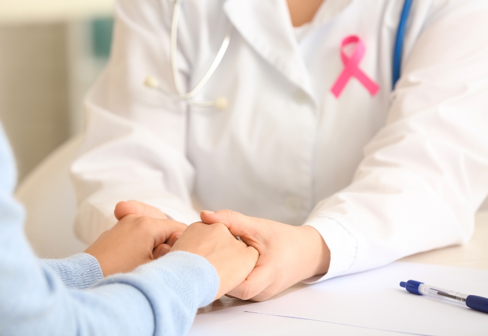 medical person in white jacket with pink ribbon holding hands of patient