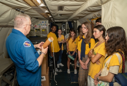 Richard G. Henning, senior flight director at the NOAA Aircraft Operations Center, on his last day before he retired spent time with the Weather, Climate, and Society REU students showing them the dropsonde, an instrument deployed from a plane, to collect atmospheric measurements inside a hurricane. (Photo by Corey Lepak)