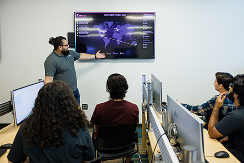 instructor does presentation on wall monitor in front of students