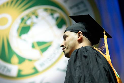 graduate in cap and gown stands in front of USF seal